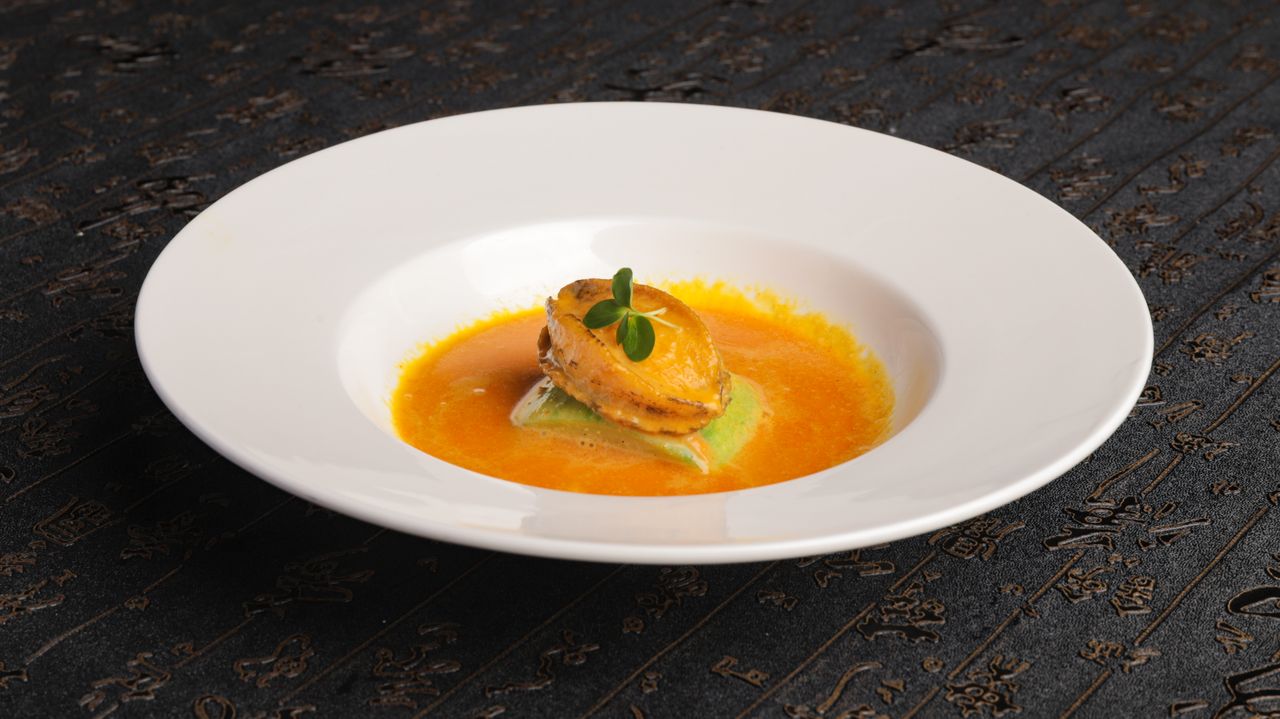 Elegant seafood dish featuring a mussel in vibrant orange sauce served on a white plate.