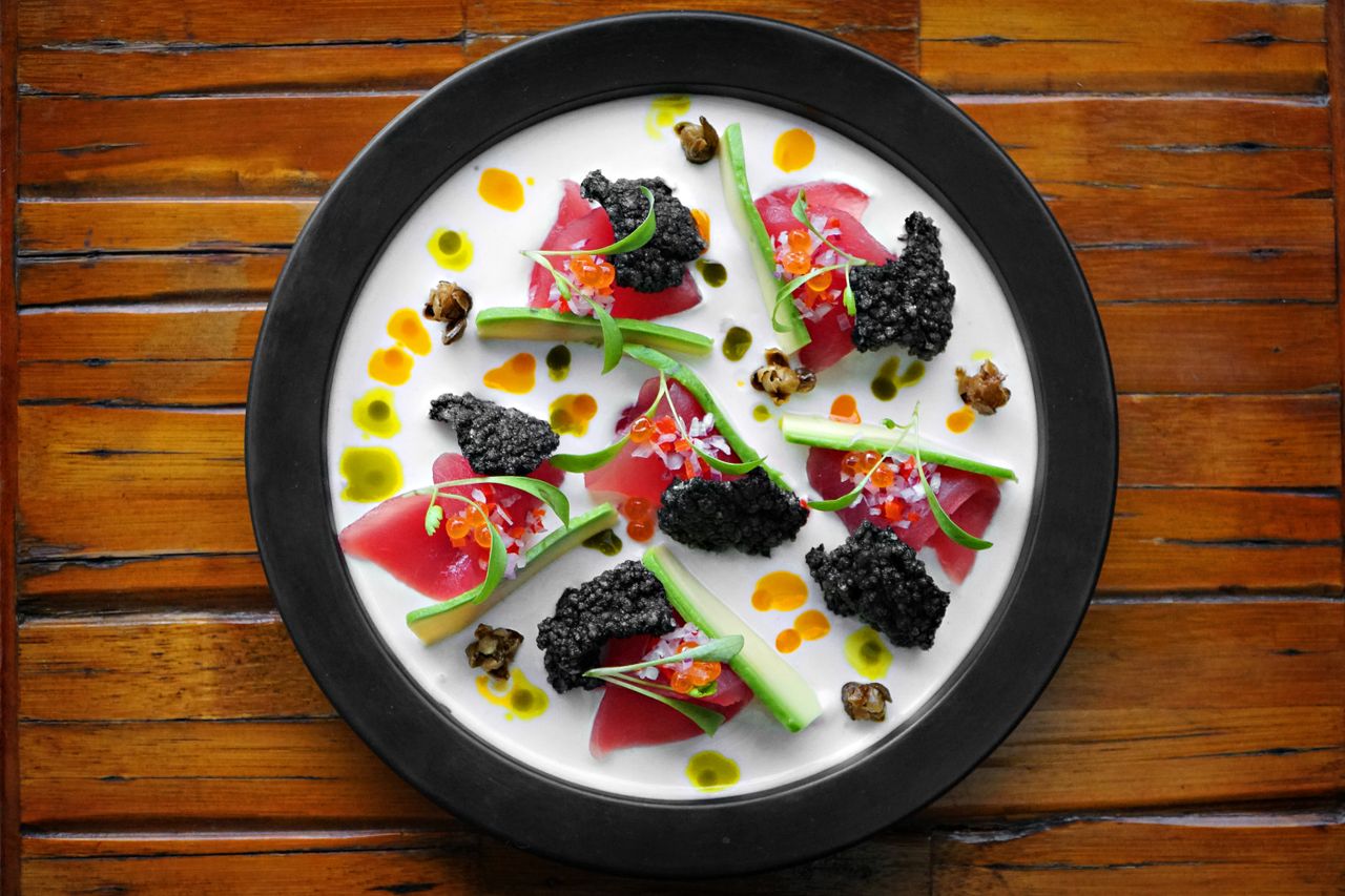 Exquisite plated dish with tuna, caviar, and vibrant garnishes on wood table.